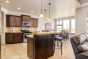 Kitchen with appliances with stainless steel finishes, open floor plan, a kitchen bar, tasteful backsplash, and a chandelier