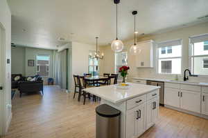Kitchen featuring dishwasher, light wood finished floors, a kitchen island, a textured ceiling, and white cabinetry