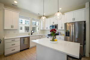 Kitchen with stainless steel appliances, light wood-type flooring, white cabinets, recessed lighting, and light countertops