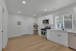 Kitchen with appliances with stainless steel finishes, light wood finished floors, white cabinetry, light countertops, and recessed lighting