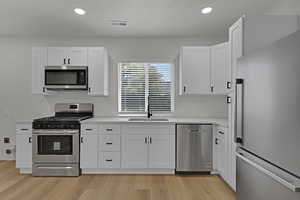 Kitchen with stainless steel appliances, light countertops, white cabinets, recessed lighting, and light wood-style floors