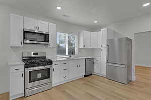 Kitchen featuring appliances with stainless steel finishes, light countertops, light wood-style flooring, white cabinets, and recessed lighting