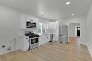 Kitchen with appliances with stainless steel finishes, light countertops, white cabinets, light wood-style flooring, and recessed lighting