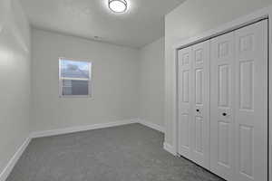 Unfurnished bedroom featuring a textured ceiling, dark carpet, and a closet
