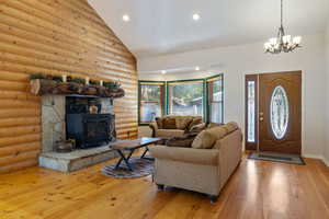 Living area with rustic walls, hardwood / wood-style floors, high vaulted ceiling, a chandelier, and a wood stove