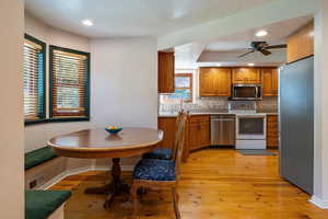 Kitchen featuring appliances with stainless steel finishes, brown cabinets, decorative backsplash, ceiling fan, and light wood finished floors
