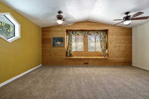 Bonus room with wood walls, vaulted ceiling, carpet floors, a ceiling fan, and a textured ceiling