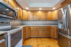 Kitchen featuring stainless steel appliances, brown cabinets, light wood-type flooring, decorative backsplash, and light countertops