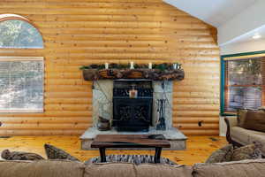 Living room featuring hardwood / wood-style flooring, rustic walls, high vaulted ceiling, and a wood stove