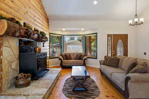 Living area with light wood-style flooring, a wood stove, a chandelier, lofted ceiling, and recessed lighting