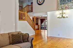 Living room with stairs, a chandelier, wood finished floors, and a high ceiling