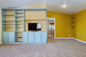 Unfurnished living room featuring light colored carpet and vaulted ceiling