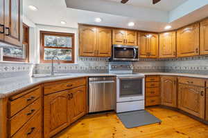 Kitchen with stainless steel appliances, brown cabinets, light wood finished floors, decorative backsplash, and recessed lighting