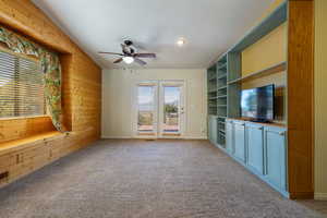 Unfurnished living room with carpet floors, a ceiling fan, wooden walls, and lofted ceiling