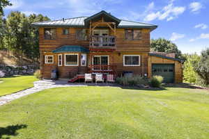 Rear view of property featuring a balcony, a standing seam roof, a lawn, an attached garage, and a metal roof