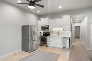 Kitchen featuring appliances with stainless steel finishes, light countertops, ceiling fan, backsplash, and white cabinetry