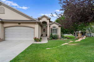 View of front facade with stucco siding, concrete driveway, a front yard, and an attached garage