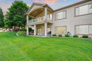 Back of house at dusk with a balcony, a patio area, stucco siding, and a yard