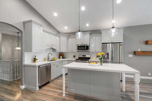 Kitchen featuring appliances with stainless steel finishes, backsplash, a kitchen breakfast bar, wood finished floors, and vaulted ceiling