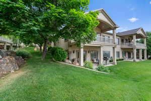 Back of house featuring a balcony, a yard, a patio, and stucco siding