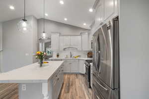 Kitchen featuring appliances with stainless steel finishes, wood finished floors, white cabinetry, tasteful backsplash, and lofted ceiling