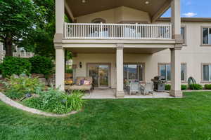 Rear view of house featuring a balcony, stucco siding, and a yard