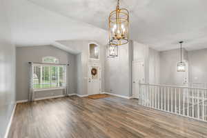 Entrance foyer featuring vaulted ceiling, a chandelier, and wood finished floors