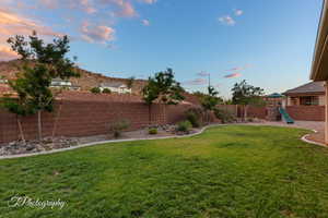 Yard at dusk featuring a playground and a fenced backyard