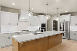 Kitchen with stainless steel appliances, premium range hood, light countertops, a kitchen bar, and recessed lighting