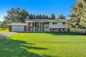 Raised ranch with driveway, an attached garage, a front yard, and a chimney