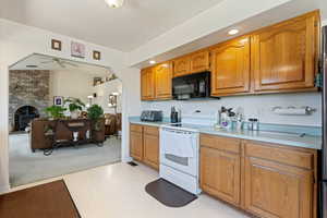 Kitchen with black microwave, white electric range oven, a ceiling fan, light countertops, and brown cabinetry
