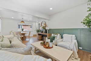 Living room featuring wood finished floors, a decorative wall, recessed lighting, and wainscoting