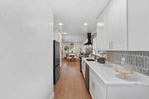 Kitchen with wall chimney exhaust hood, stainless steel appliances, white cabinetry, light wood-style floors, and recessed lighting