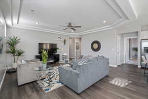 Living room with a raised ceiling, a ceiling fan, dark wood-style floors, and recessed lighting