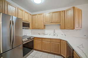 Kitchen featuring appliances with stainless steel finishes, light tile patterned floors, a textured ceiling, light stone counters, and light brown cabinets