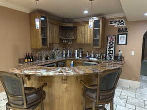 Indoor wet bar with crown molding, stone tile floors, hanging light fixtures, arched walkways, and recessed lighting