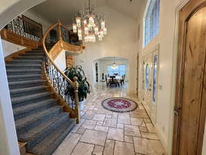 Entryway featuring a chandelier, stone tile flooring, arched walkways, stairs, and high vaulted ceiling