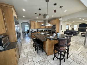 Kitchen with stainless steel appliances, island exhaust hood, arched walkways, a kitchen breakfast bar, and ornamental molding