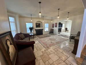 Living area featuring a fireplace, arched walkways, stone tile floors, healthy amount of natural light, and crown molding