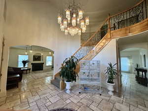 Stairs featuring arched walkways, stone tile floors, a towering ceiling, a fireplace, and a chandelier