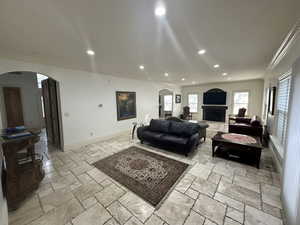 Living area featuring crown molding, arched walkways, recessed lighting, stone tile floors, and a fireplace