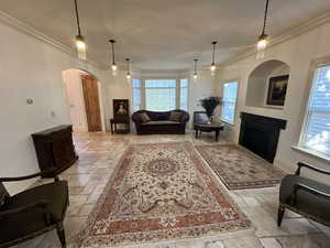 Living room with stone tile flooring, arched walkways, crown molding, and a fireplace