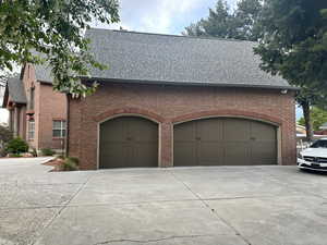 View of side of home featuring brick siding, concrete driveway, a garage, and roof with shingles