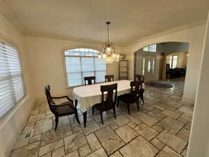 Dining room featuring stone tile floors, arched walkways, a chandelier, and crown molding