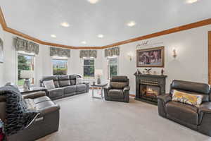 Carpeted living area featuring crown molding, a glass covered fireplace, a textured ceiling, and recessed lighting
