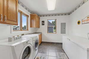 Washroom with cabinet space, electric panel, washer and clothes dryer, and light tile patterned floors