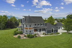 Rear view of house featuring covered porch, a shingled roof, concrete driveway, and a yard