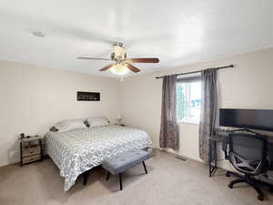Bedroom with light colored carpet, ceiling fan, and a desk
