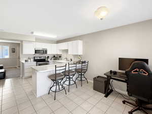 Kitchen with stainless steel appliances, a peninsula, a kitchen breakfast bar, light countertops, and white cabinets