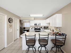Kitchen featuring appliances with stainless steel finishes, a peninsula, white cabinets, light countertops, and a breakfast bar